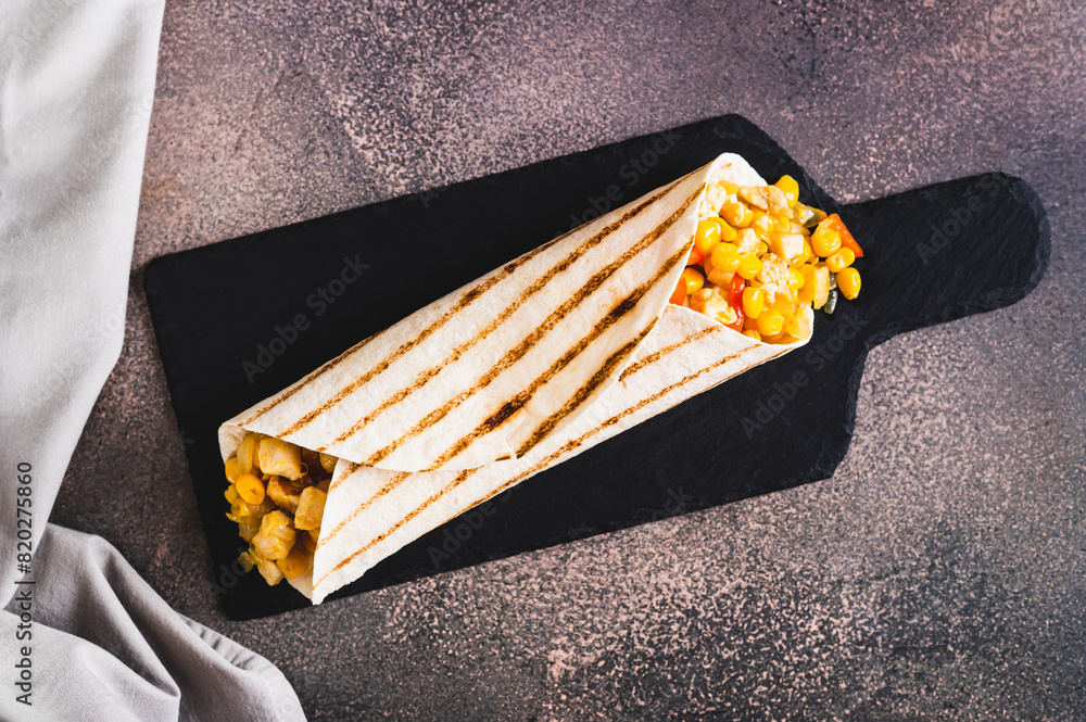 Wall mural Close up of mexican Burrito with corn, chicken and peppers in a tortilla on a slate board top view - Wall murals