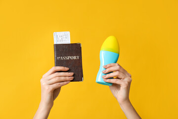 Female hands with passport and bottle of sunscreen cream on yellow background. Travel concept