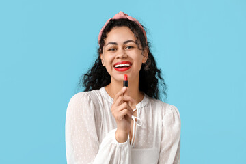 Happy young African-American woman with red lipstick on blue background