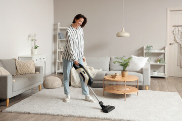 Happy young woman cleaning carpet with handheld vacuum cleaner in living room