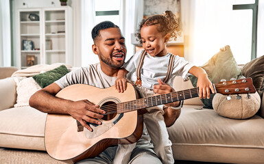 Happy dad and daughter playing the guitar. Little cute girl dancing at home in the living room. Time together.
