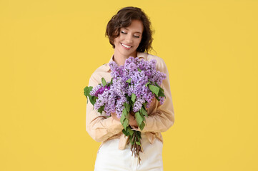 Beautiful young woman with bouquet of blooming lilac flowers on yellow background
