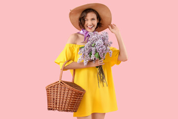 Beautiful young woman with bouquet of blooming lilac flowers and wicker basket on pink background