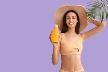 Beautiful young woman in wicker hat with bottle of sunscreen cream and palm leaf on lilac background
