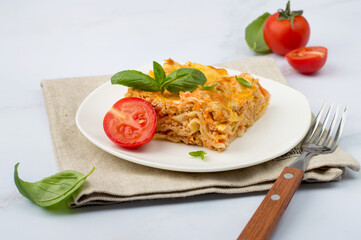 Traditional Italian dish of lasagna with bolognese sauce garnished with basil and tomatoes on a white plate. Horizontal..