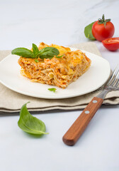 Traditional Italian dish of lasagna with bolognese sauce garnished with basil and tomatoes on a white plate..