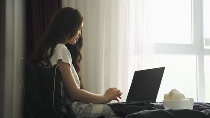 Young woman typing on the laptop and going eating marshmallows at home