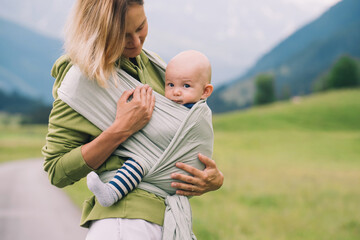 Fototapeta premium Babywearing. Mother and baby on nature outdoors. Baby in wrap carrier. Woman carrying little child in baby sling in green mint color. Concept of green parenting, natural motherhood, postpartum period.