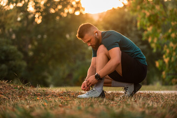 A young athletic man tying running shoes with wireless earphones listening a music for motivation...