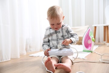 Little child playing with power strip and iron plug on floor at home. Dangerous situation