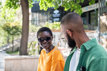 Happy loving african american couple met on street, sitting together, smiling, chatting, enjoy company, attracted to each other. Joyful black stylish girl and guy students talking outdoor after study