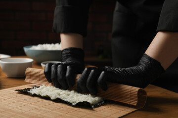 Chef in gloves making sushi roll at wooden table, closeup
