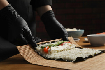 Chef in gloves making sushi roll at wooden table, closeup