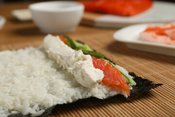 Unwrapped sushi roll with rice, cucumber, cheese and salmon on bamboo mat, closeup