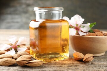 Almond oil in bottle, flowers, bowl and nuts on wooden table, closeup