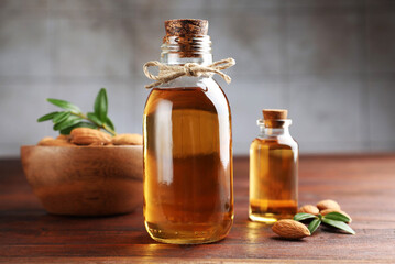 Almond oil in bottles, leaves and nuts on wooden table, closeup