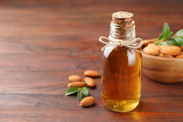 Almond oil in bottle, leaves and nuts on wooden table, closeup. Space for text