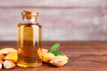 Almond oil in bottle, nuts and leaves on wooden table, closeup. Space for text
