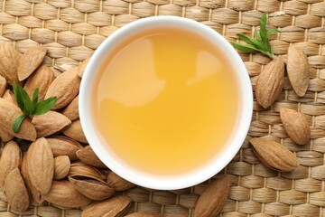 Almond oil in bowl, nuts and leaves on wicker table, flat lay