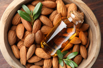 Wooden bowl with almond oil in bottle, leaves and nuts on table, top view