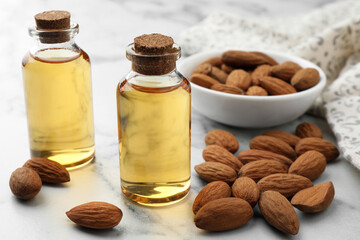 Almond oil in bottles and nuts on white marble table, closeup