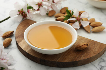 Almond oil in bowl, nuts and flowers on white marble table, closeup