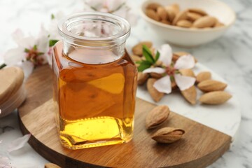 Almond oil in bottle, nuts and flowers on white marble table, closeup