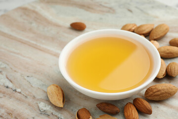 Almond oil in bowl and nuts on color marble table, closeup. Space for text