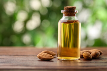 Almond oil in bottle and nuts on wooden table against blurred green background, closeup. Space for text