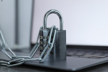 Cyber security. Metal combination padlock with chain and laptop on table, closeup