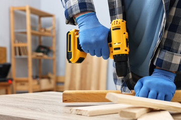 Young handyman working with electric drill at table in workshop, closeup