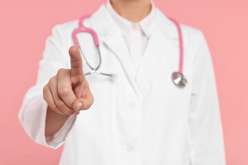 Doctor with stethoscope pointing on pink background, closeup