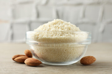 Fresh almond flour in bowl and nuts on wooden table, closeup