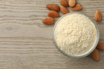 Fresh almond flour in bowl and nuts on wooden table, top view. Space for text