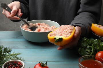 Woman making stuffed peppers with ground meat at light blue wooden table, closeup
