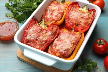Tasty stuffed peppers in dish and ingredients on light blue wooden table, closeup