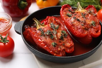 Tasty stuffed peppers in dish and ingredients on white tiled table, closeup