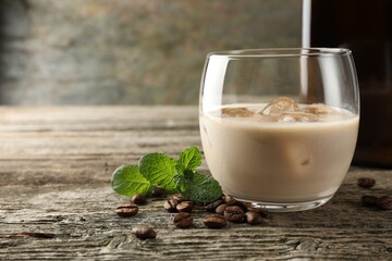 Coffee cream liqueur in glass, mint and beans on wooden table, closeup. Space for text
