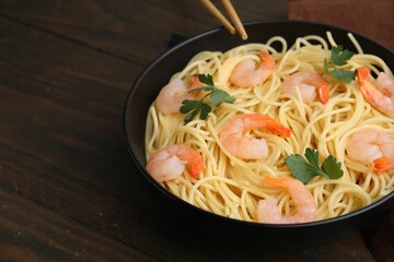 Tasty spaghetti with shrimps and parsley in bowl on wooden table, closeup. Space for text