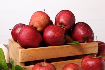 Fresh red apples with water drops in wooden crate on white background, closeup