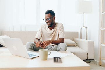Smiling African American Man Working on Laptop in Modern Home Office at the Sofa
