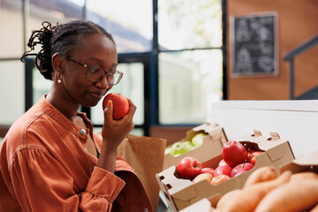 African american customer grasping and smelling fresh red apple, choosing best product in eco...