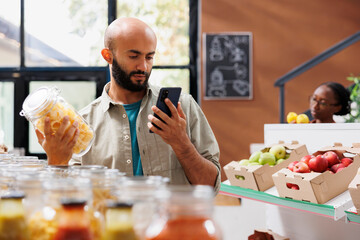 Bearded man in closeup using smartphone to search for recipes and prices at nearby eco friendly...