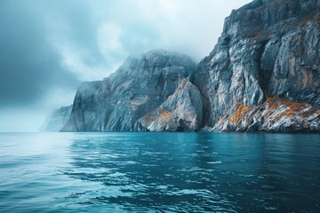 A rocky mountain juts out from the water, contrasting with the serene blue ocean beneath a dramatic gray-blue sky. This picturesque seascape captures the beauty of nature in its raw and majestic form.