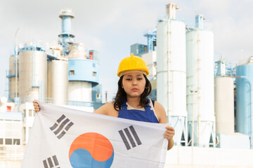 Portrait of sad teenage girl in blue overalls with flag of South Korea in her hands against the backdrop of a modern metallurgical plant