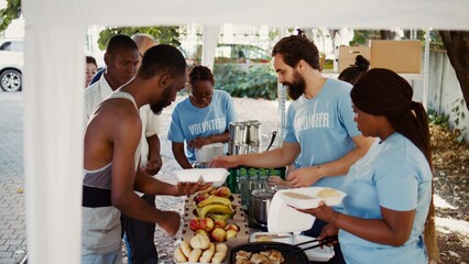 Side-view shot capturing charity workers distributing free food to homeless people and those in...