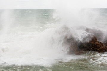 Immense sea rock covered by a large wave. Force of nature.