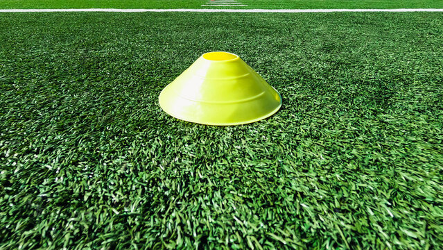 Sports Drills Training Concept. Bright yellow cone on football or soccer field turf. Horizontal white marker line in the distance, - Powered by Adobe