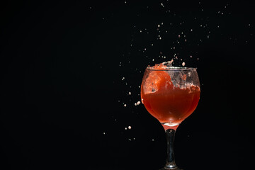 A glass cup with guava juice inside with splashes coming up. Isolated on dark background.