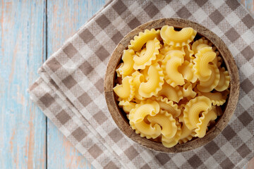 Raw Creste di Gallo Pasta in Wooden Bowl on Linen Napkin, Top View, Copy Space